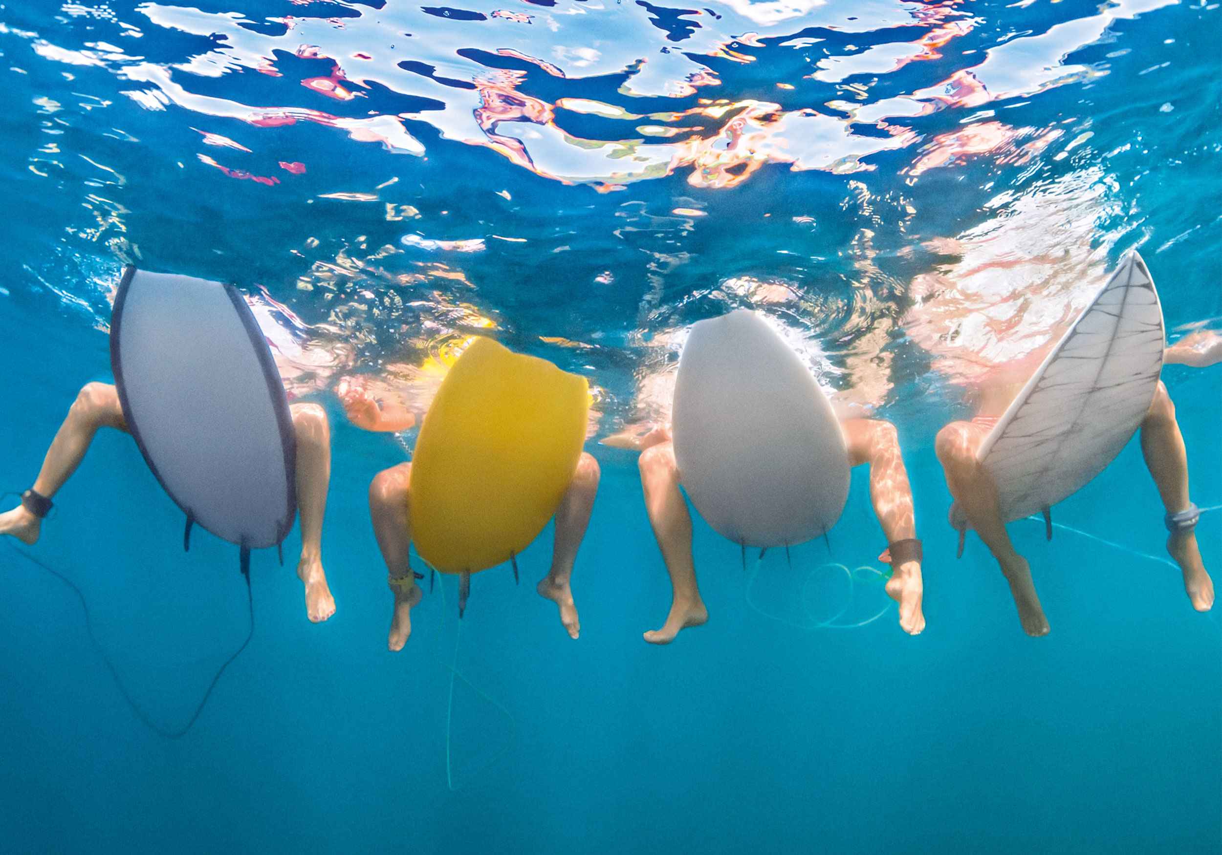 Unterwasserperspektive vier Surfer sitzen auf Surfboards 