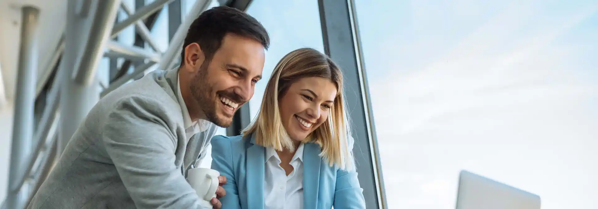 Mann und Frau im Anzug schauen lächelnd auf Laptop