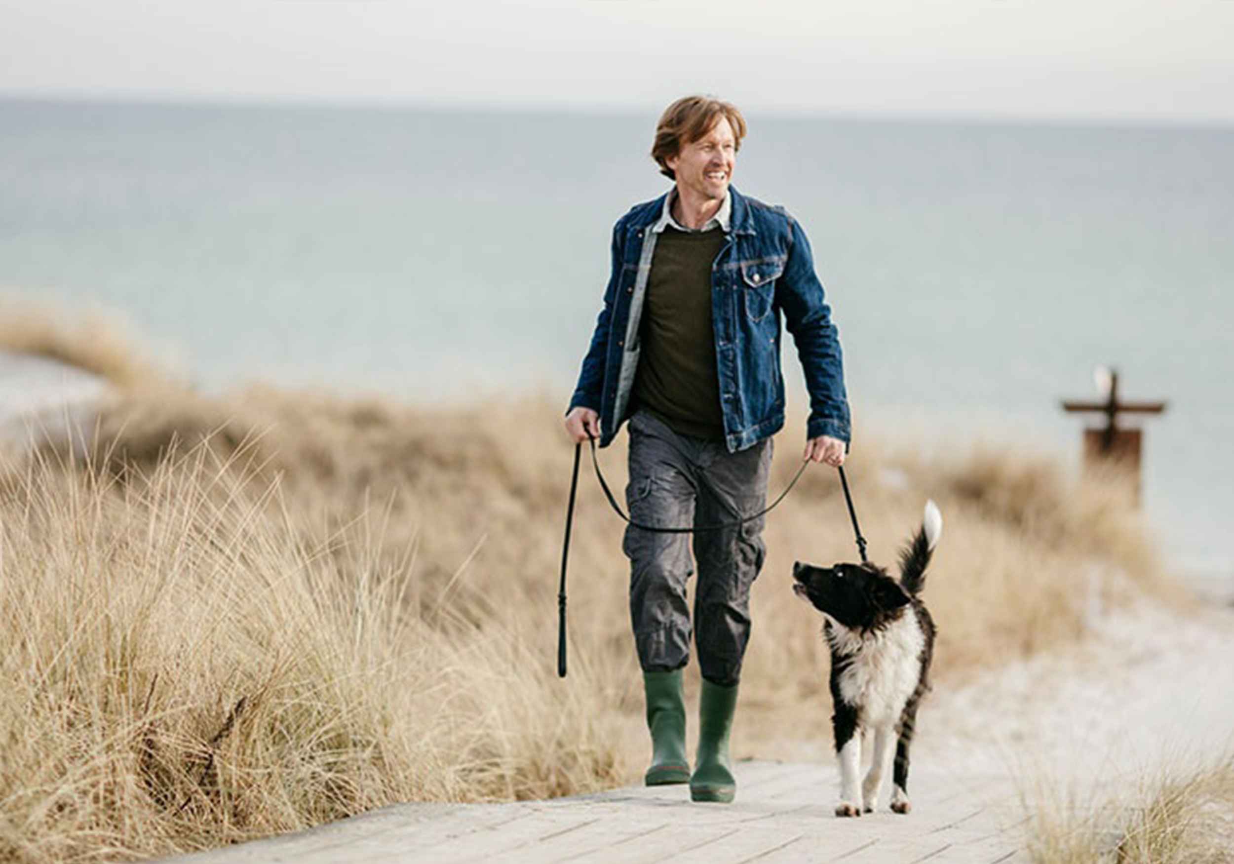 Mann läuft lächelnd mit Hund am Meer 